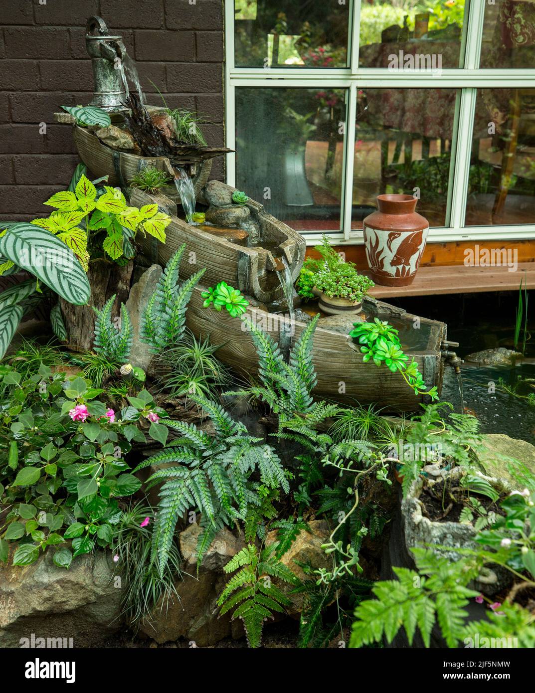 Unusual garden water feature, waterfall made from old wooden barrels surrounded by a rockery with emerald green ferns and other plants Stock Photo