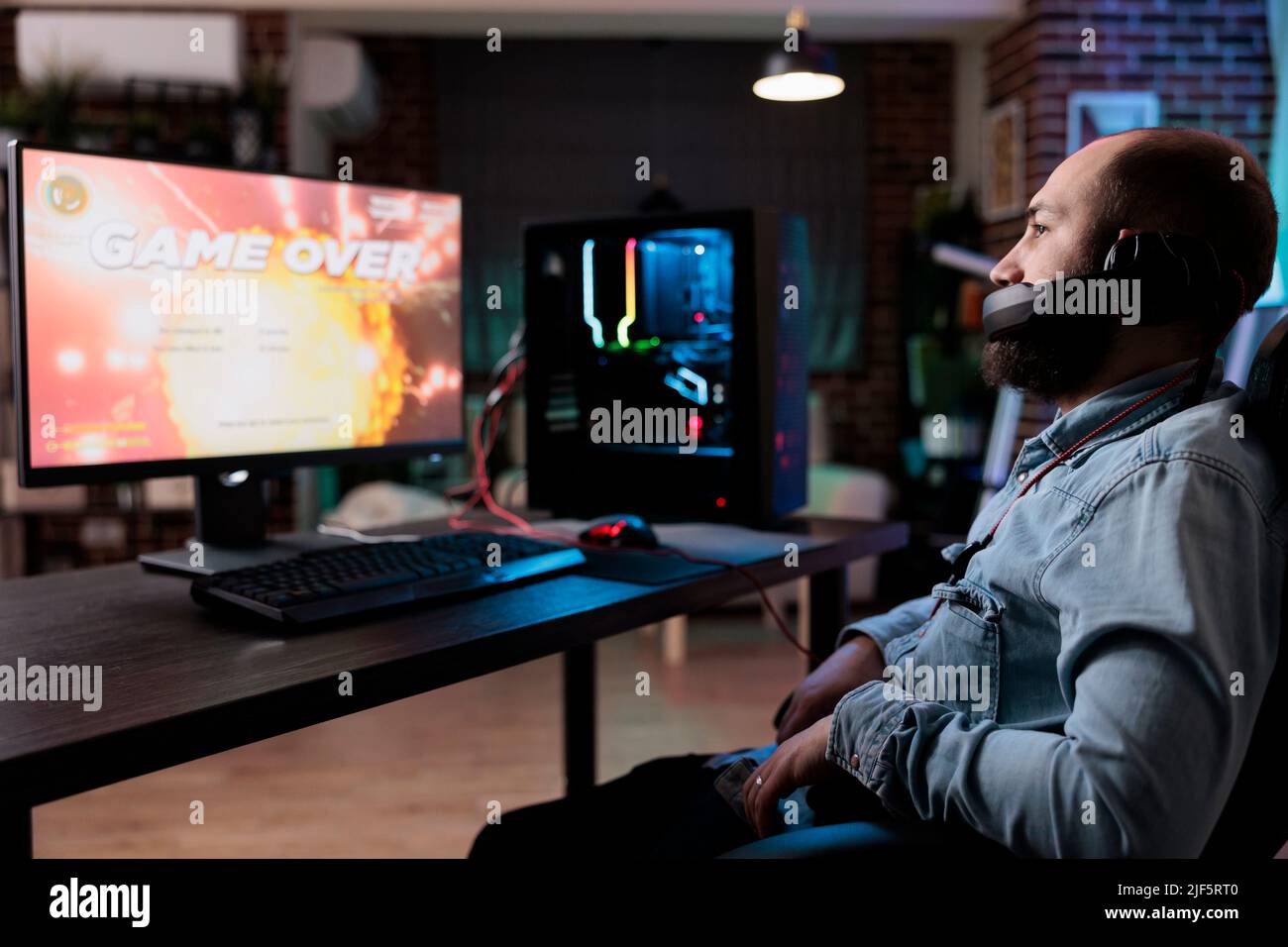 Caucasian man feeling frustrated about lost video games play using online streaming platform on computer. Male gamer playing action game and losing internet rpg tournament at desk with neon lights. Stock Photo