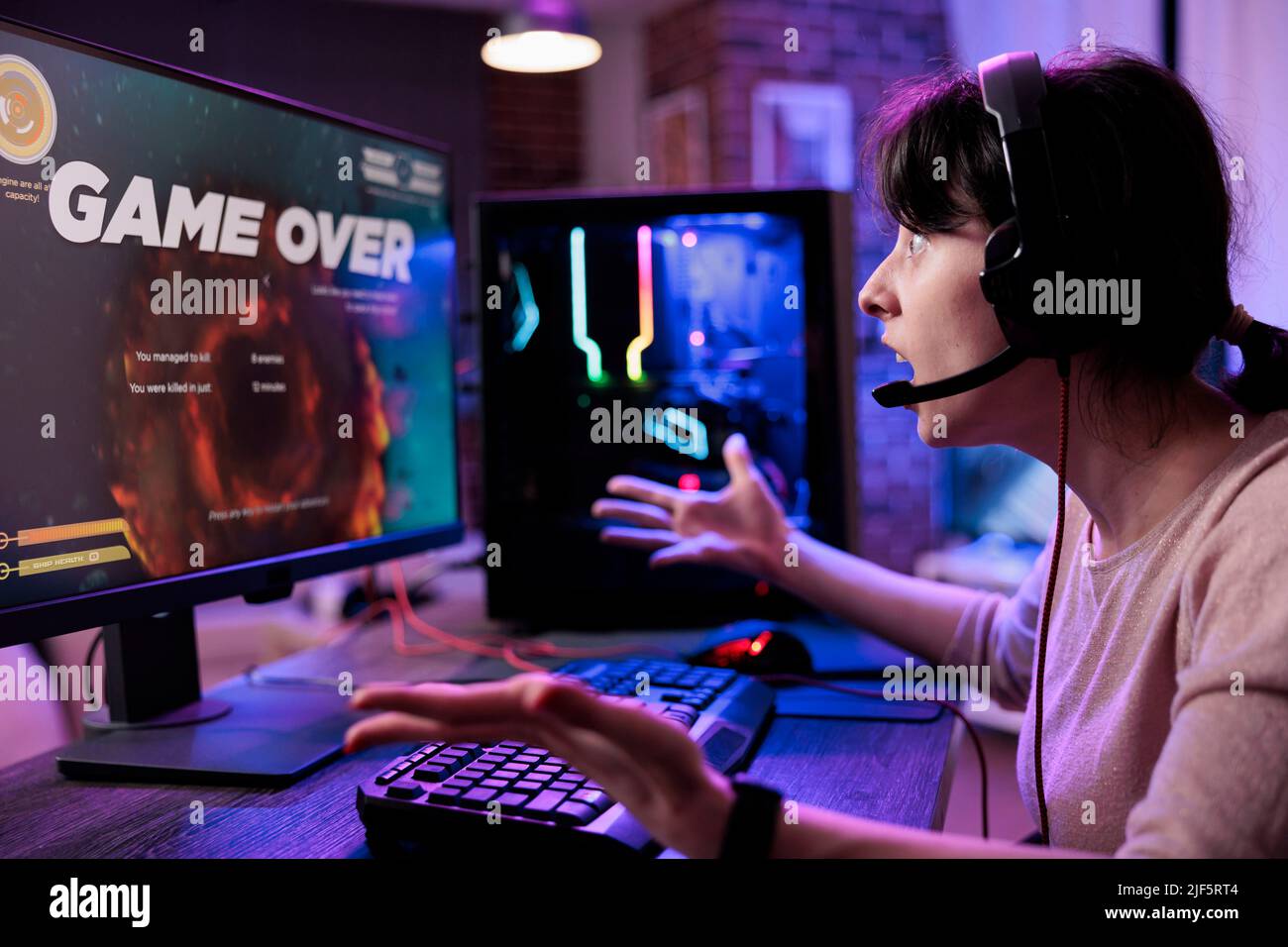 Young player losing video games tournament on computer, feeling sad about lost shooting gameplay competititon. Female gamer playing online rpg action championship on live stream. Stock Photo