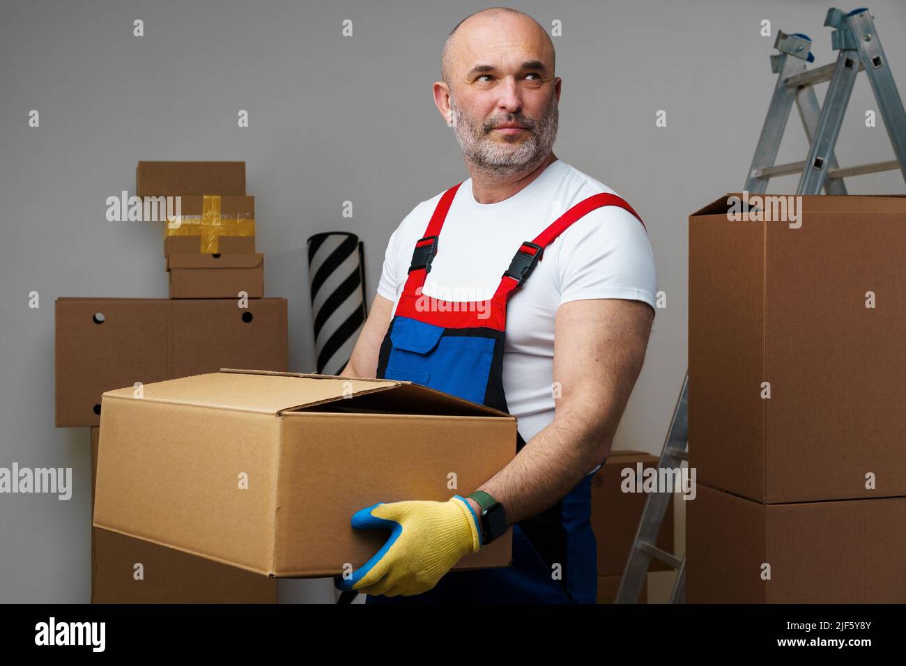 Middle-aged man mover in uniform holding cardboard box, portrait Stock Photo