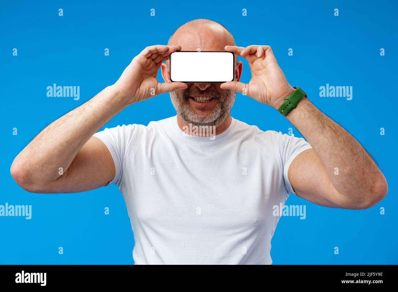 Middle-aged man holding blank smartphone on his eyes in studio Stock Photo