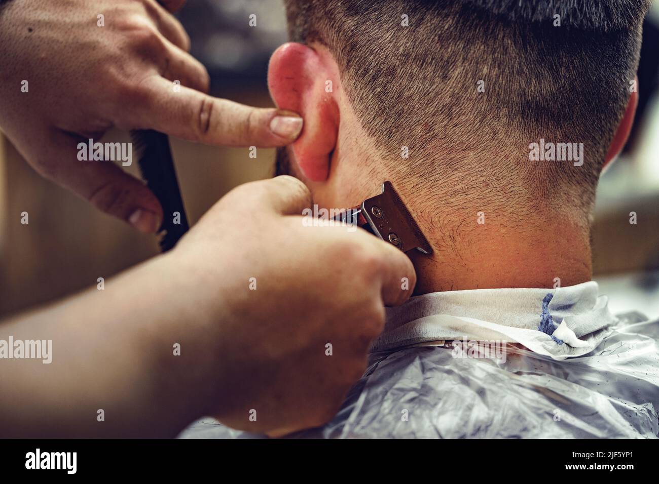 Barber guy gives a haircut to a bearded man sitting in a chair in a barbershop Stock Photo