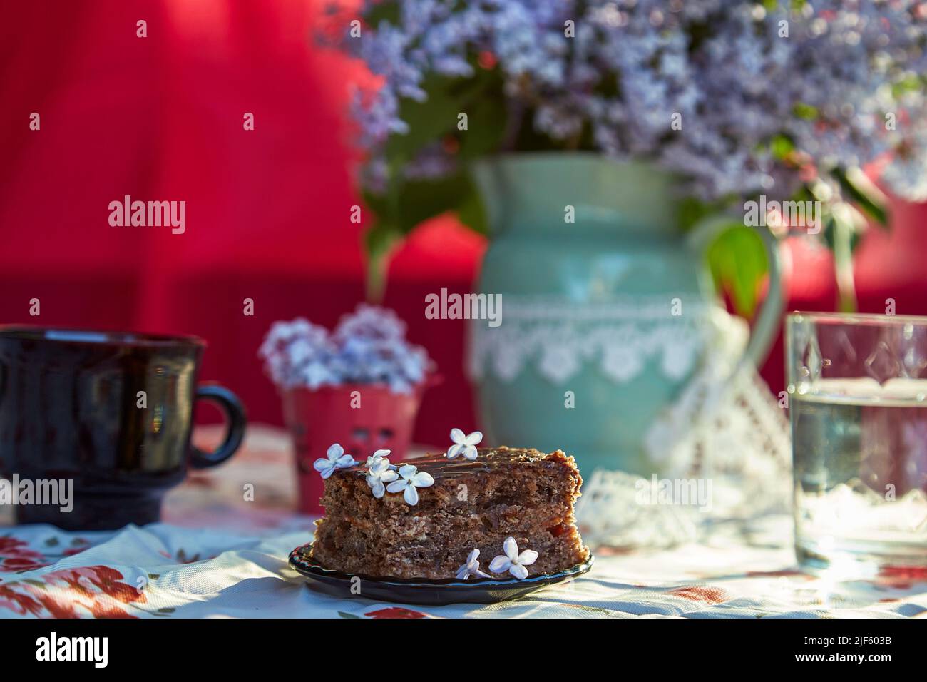 Aesthetic homemade chocolate cake. Dessert and cup of coffee among flowers. Atmospheric breakfast.  Stock Photo