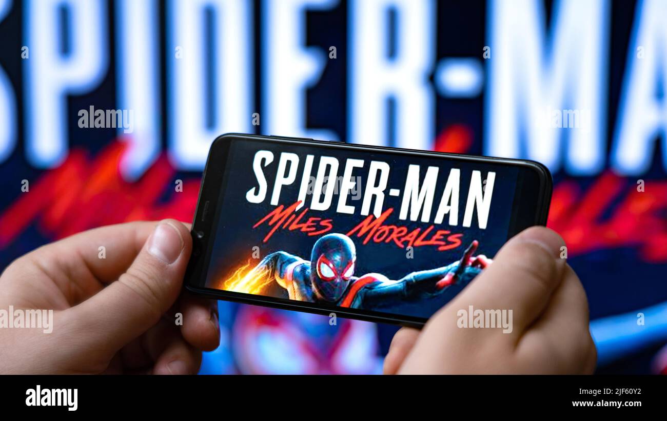 Nova Lima, Brazil - June 2022: Hands holding a smartphone with Spider-Man Miles Morales: Android Edition in front of a big screen. Stock Photo