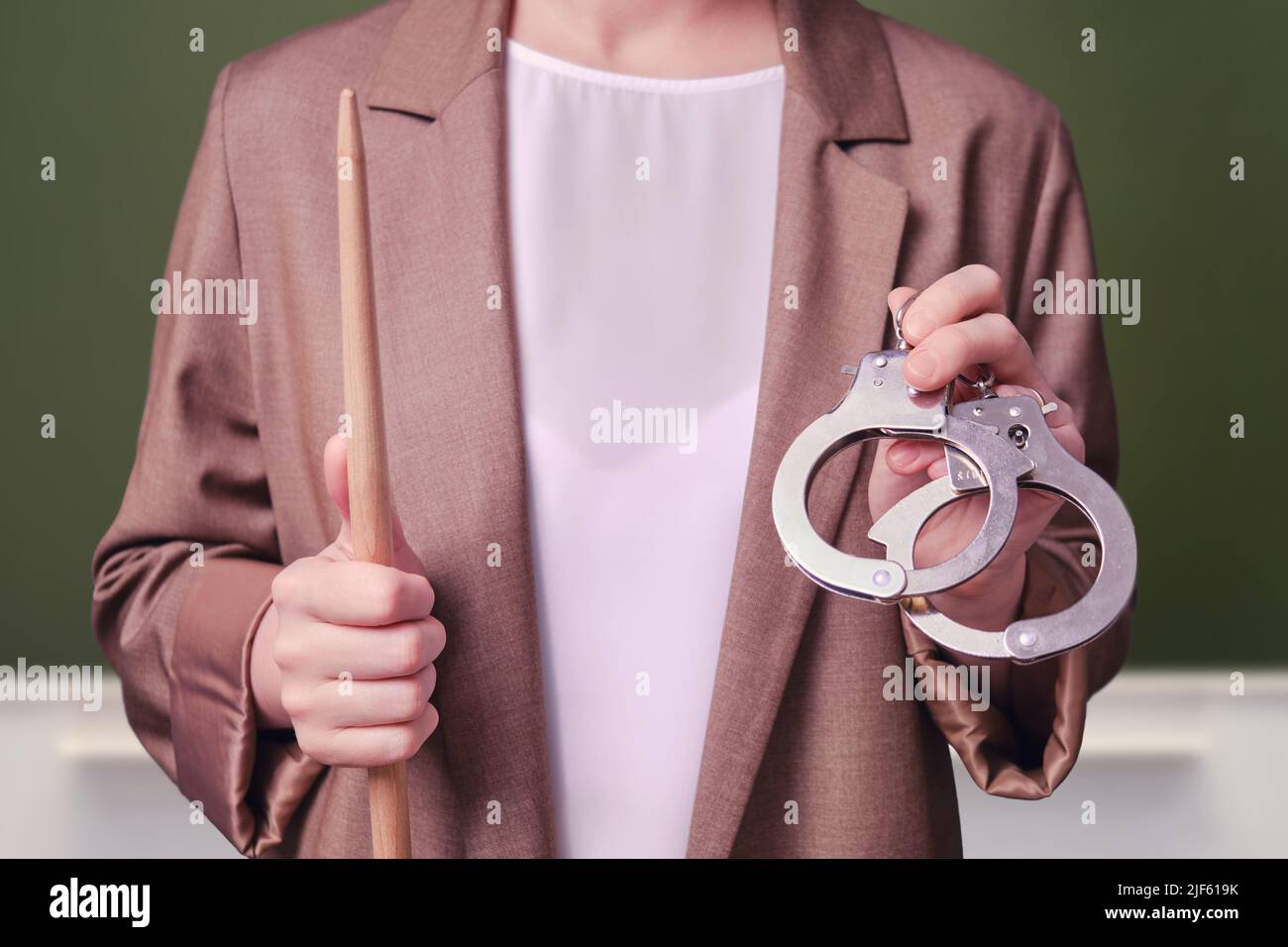Woman teacher holding handcuffs in her hands on school blackboard in