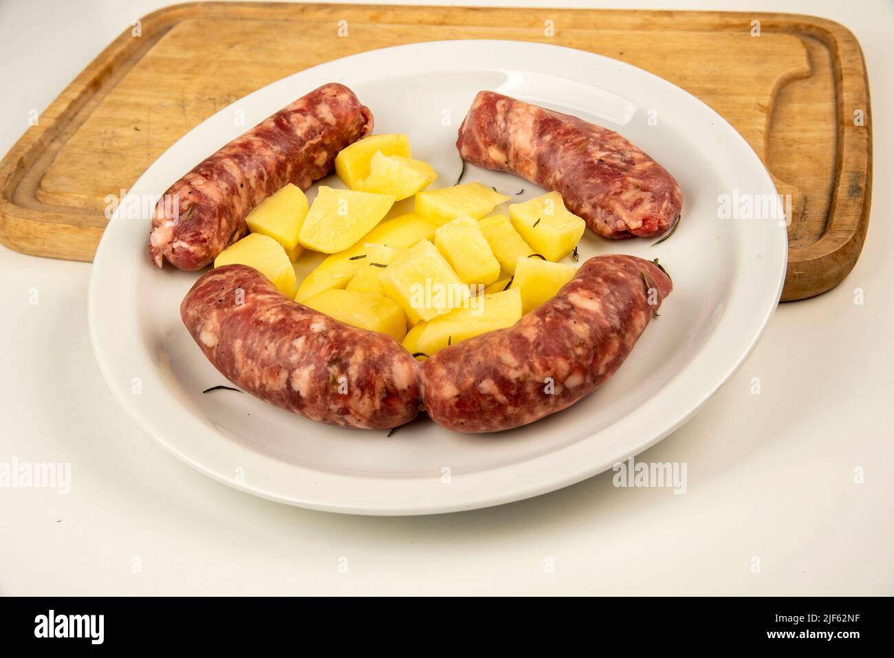 Link sausages with fresh baked potatoes on wooden cutting board   isolated on white with copy space. Stock Photo
