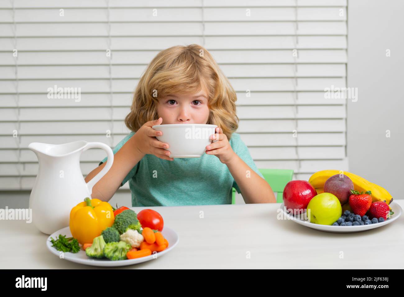 Hunger, appetite concept. Kid boy eating healthy food vegetables. Breakfast with milk, fruits and vegetables. Child eating during lunch or dinner. Stock Photo