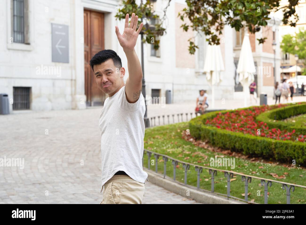 Asian man looking sad while waving hand to say goodbye to someone outdoors in the street. Stock Photo