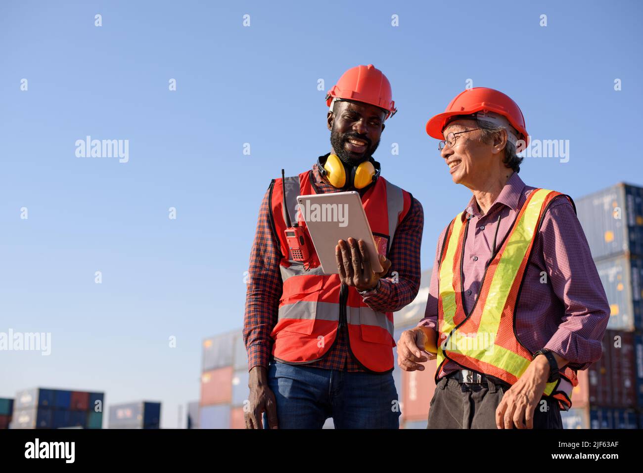 Happy African American and senior asian male worker using tablet during video call in a logistic shipping cargo containers yard. Stock Photo
