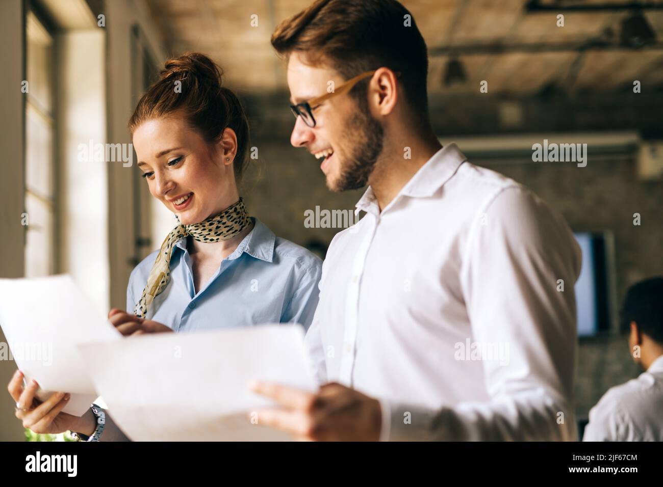 Portrait of two young business people talking about documents in office Stock Photo