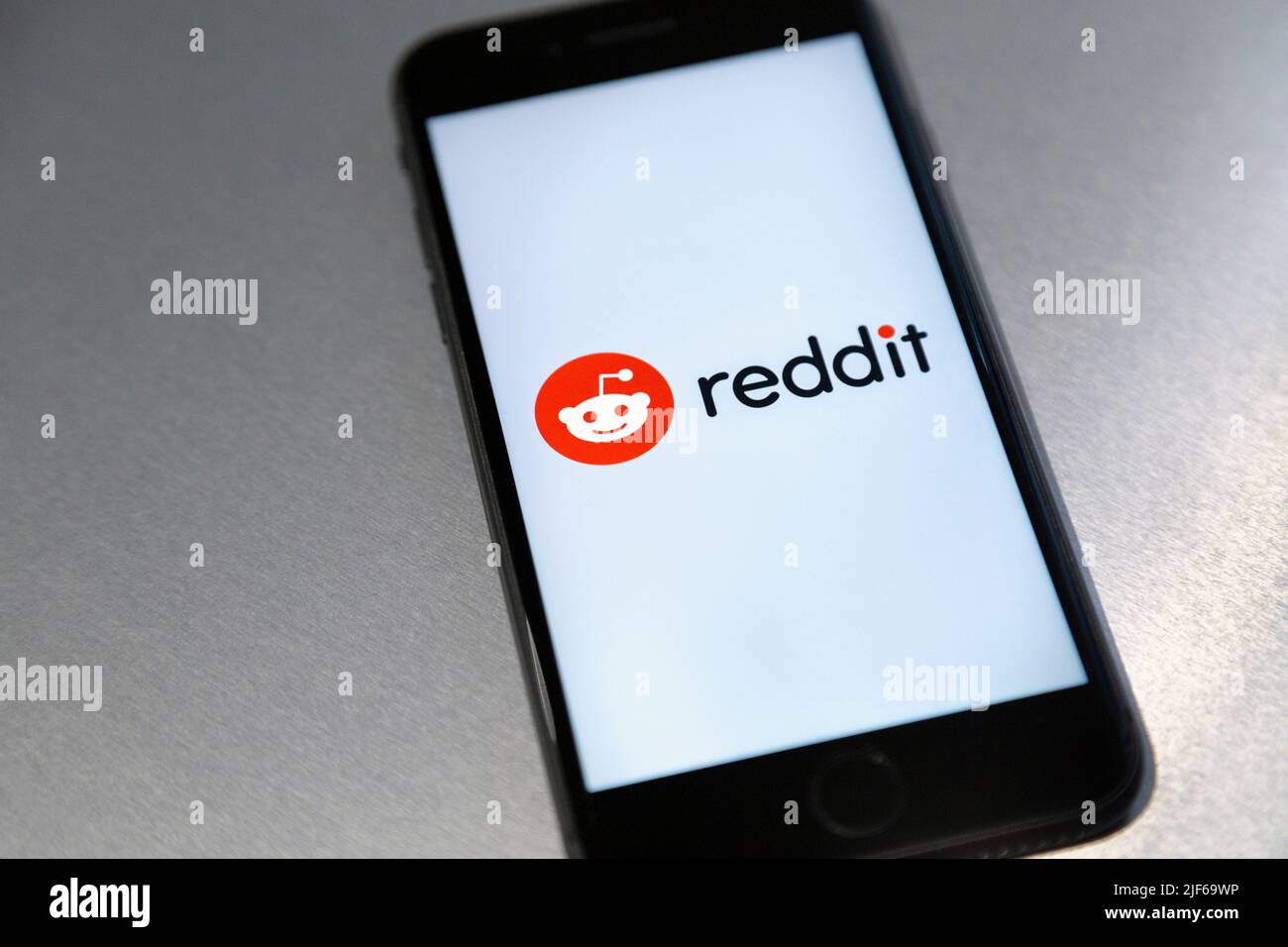 Logo of Reddit social media and news platform displayed on a phone screen against metal background Stock Photo