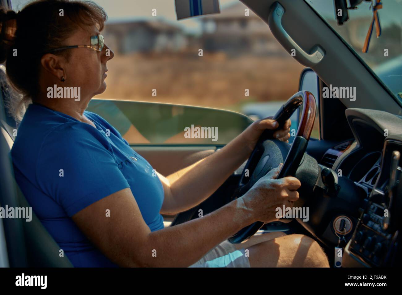 Adult mature woman with sunglasses drives a car on a sunny day Stock Photo