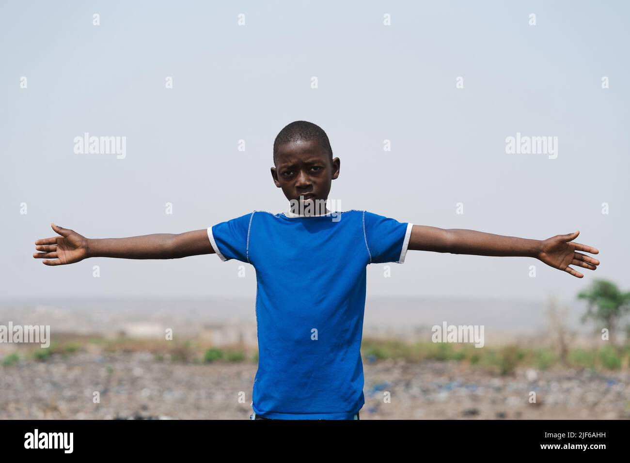 Worried African boy with outstretched arms standing in an arid field with a provocative frown on his face; global warming, climate change and deforest Stock Photo