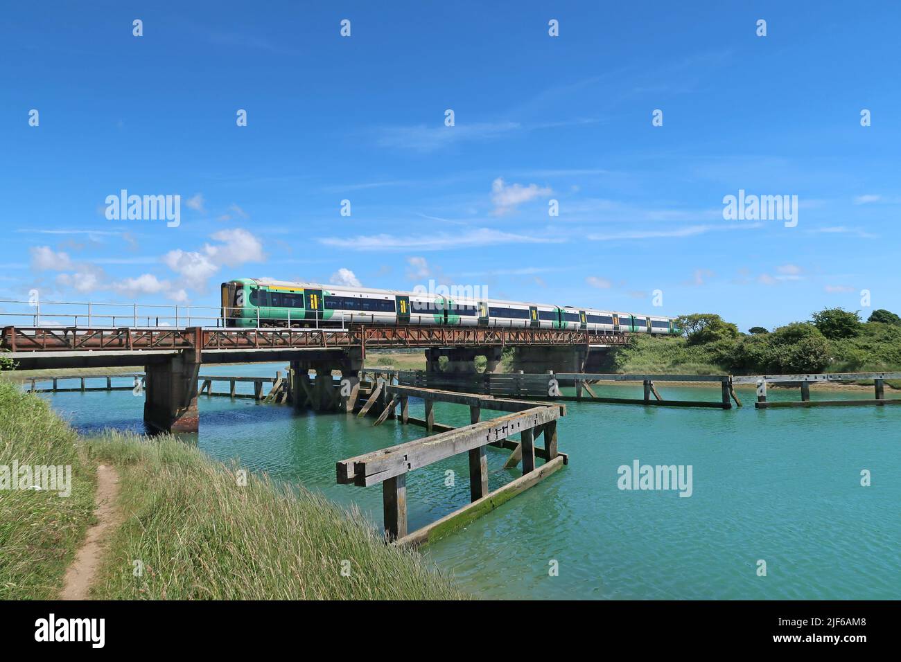 A Southern passenger train crosses the River Arun at Ford, near Littlehampton, West Sussex. Shows remains of timber jetty in foreground. Stock Photo