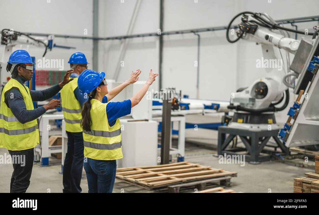Multiethnic engineers using futuristic augmented reality glasses inside robotic factory - Focus on woman face Stock Photo