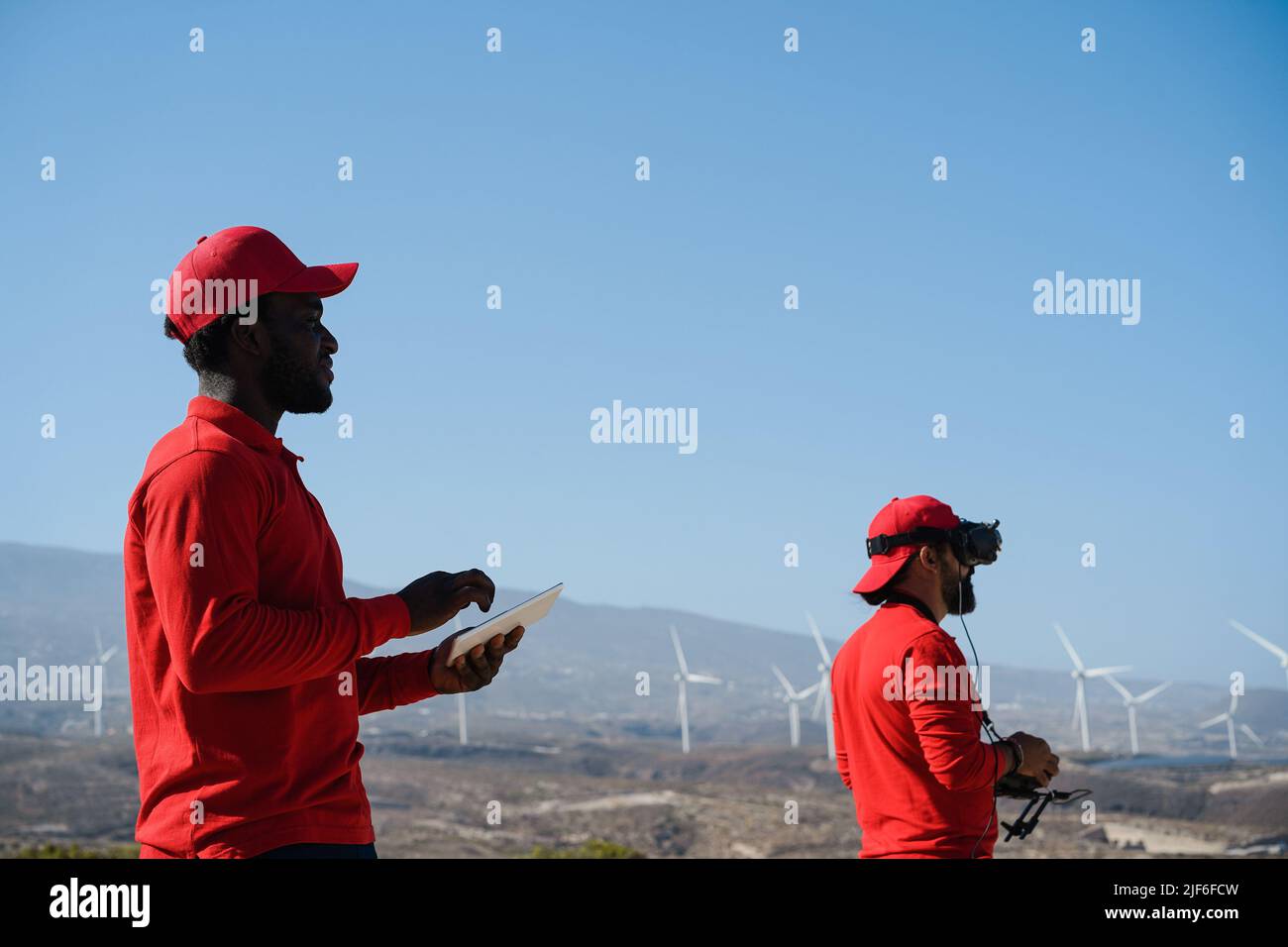 Engineers using virtual reality headset while working at windmill farm with tablet and drone - Focus on african man face Stock Photo