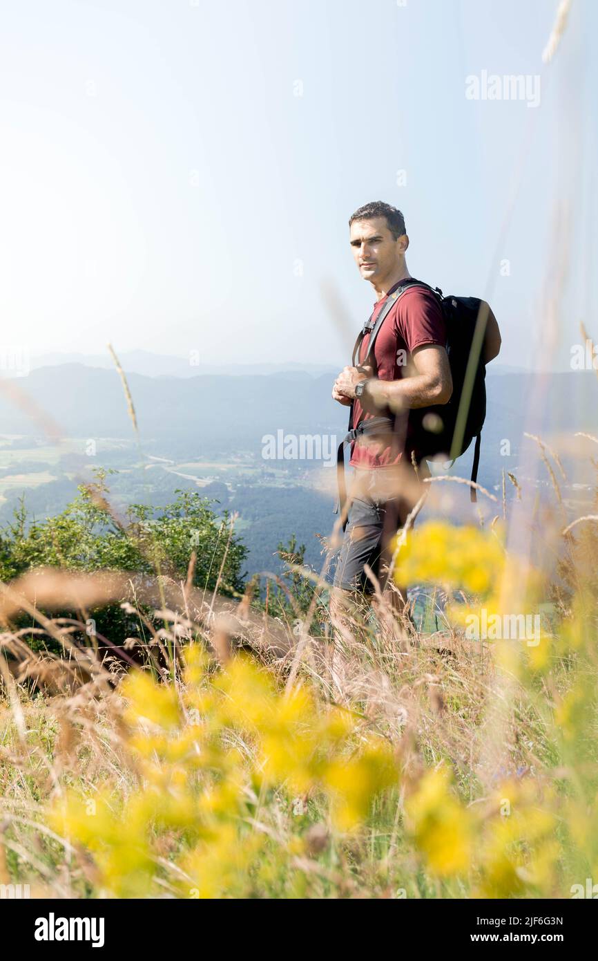 A man hiking the mountains with a backpack in the summer. Behind him is the view of the valley. Stock Photo