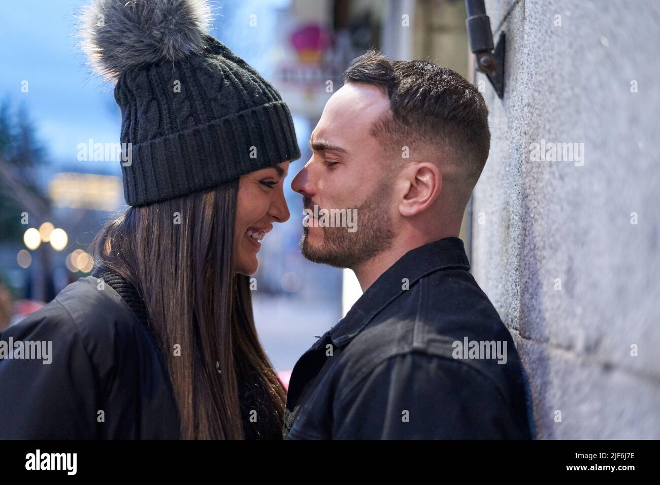 Side view of tender boyfriend with girlfriend in hat standing on street of city in evening time Stock Photo
