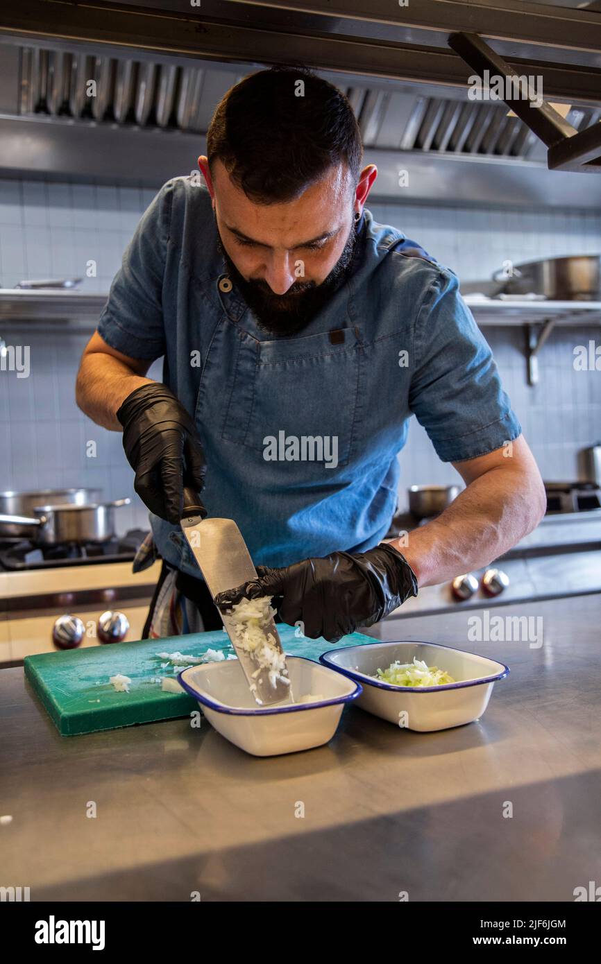 Male chef chopping fresh vegetable with knife and putting in container at commercial kitchen Stock Photo