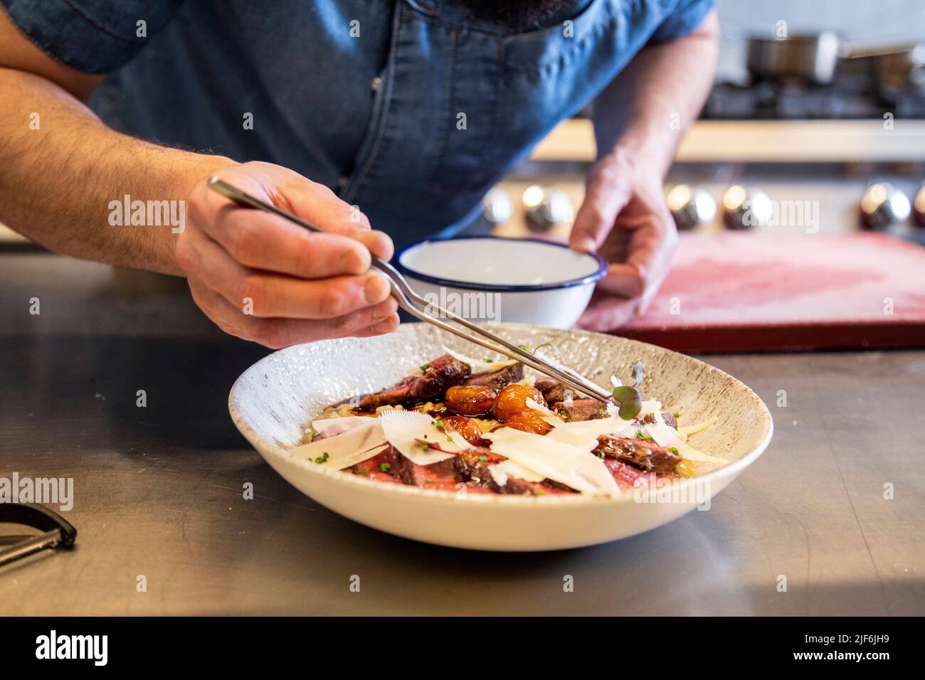 Closeup of chef garnishing herb on main dish on counter in commercial kitchen Stock Photo