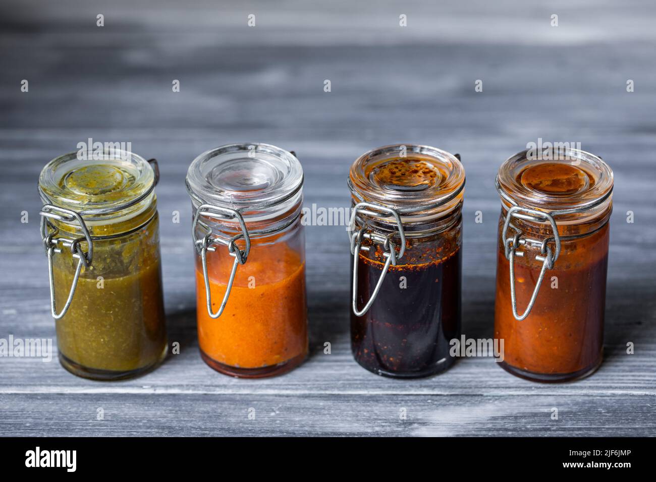 Closeup green salsa with jalapeno and avocado and habanero tatemado sauces in small glass jars placed near salsa macha with sesame and smoked chipotle Stock Photo