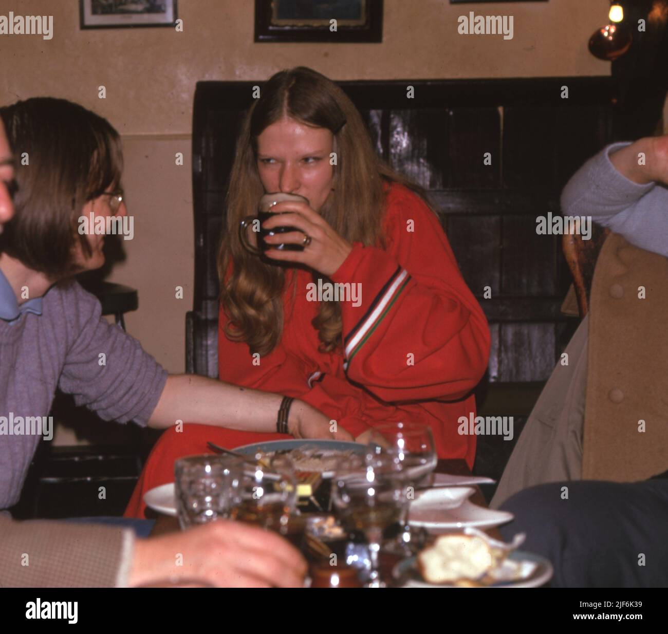A woman in a red dress enjoying a half pint of stout beer while lunching in a pub. January 1975.   Photo by Tony Henshaw Archive Stock Photo