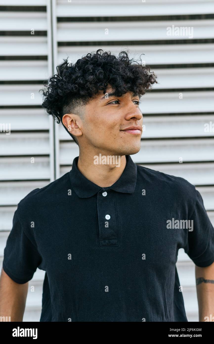 Positive man in black polo leaning on wall outside on serene summer day Stock Photo