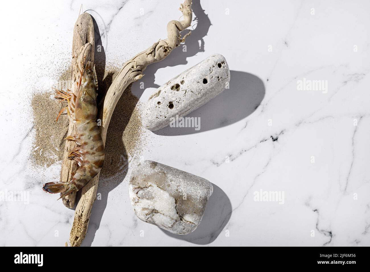 Top view of raw common prawn and driftwood sticks placed near dry sand on marble table in kitchen Stock Photo