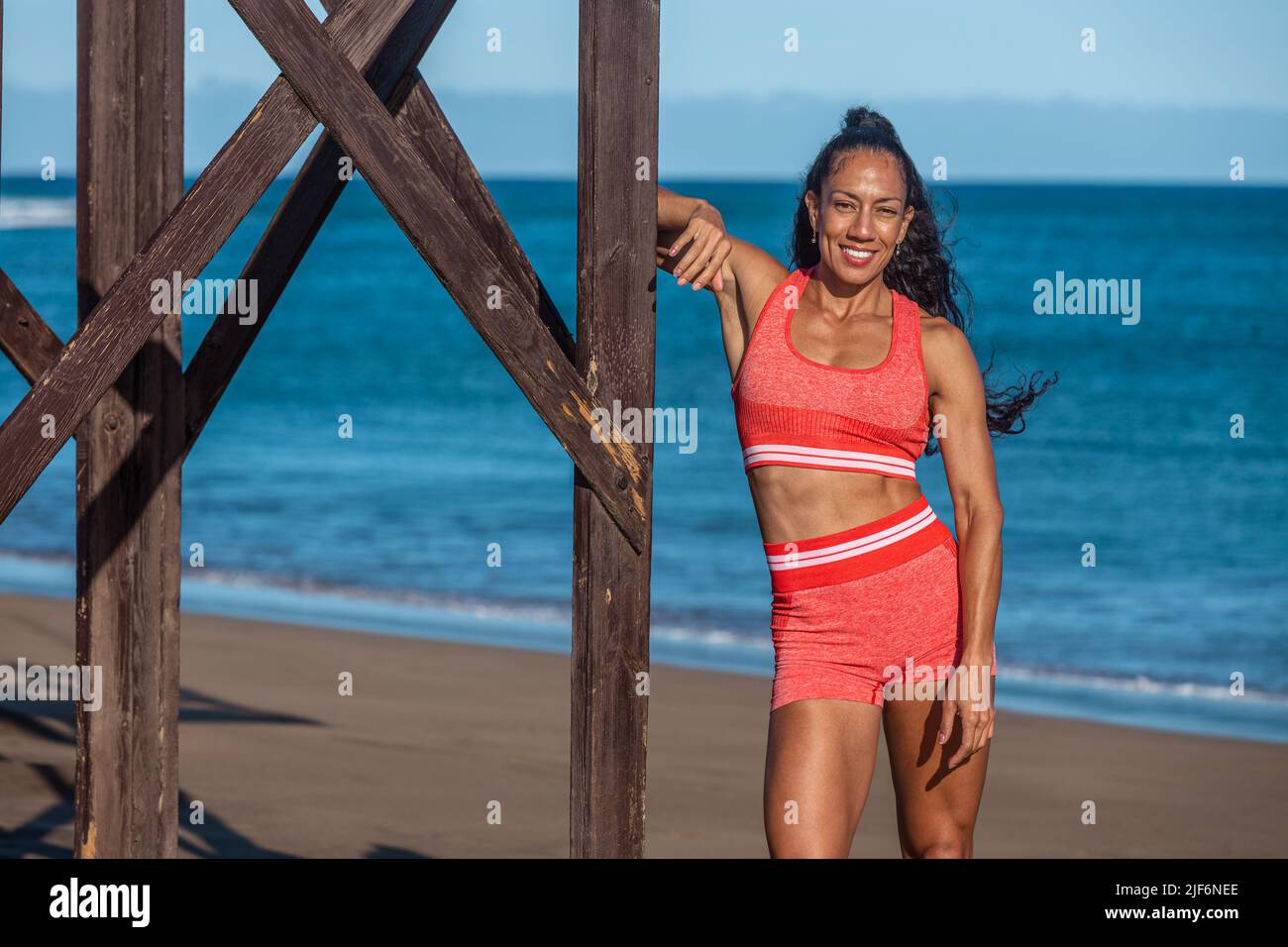 Portrait of latin female athlete in sportswear standing on beach shore during summer Stock Photo