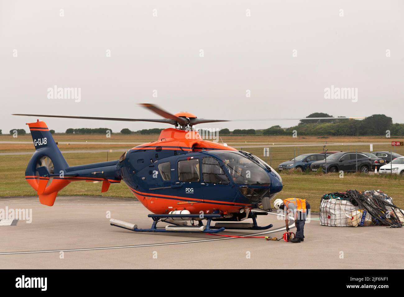 Cornwall, England, UK.2022. Airlift helicopter lifting off with cargo in a sling. Signal from ground crew staff. Stock Photo