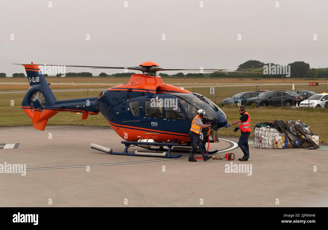 Cornwall, England, UK.2022. Airlift helicopter ground crew attaching carry strap to underbelly of aircraft and then to the cargo in a net. Stock Photo