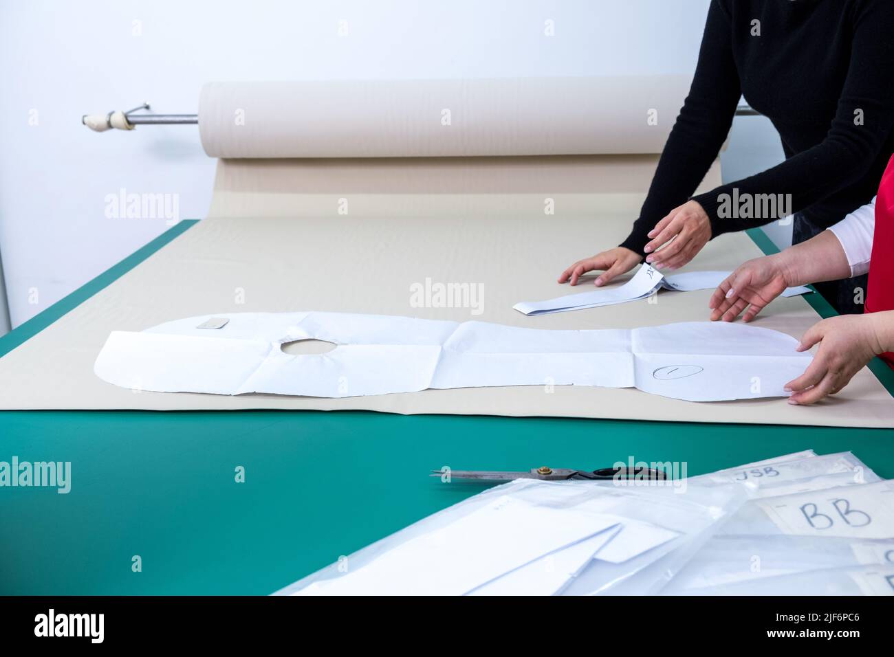 Crop anonymous dressmakers arranging paper patterns on textile while working together at table in modern light atelier with special equipment Stock Photo