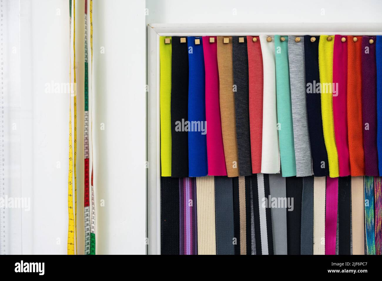 Rows of colorful textile samples hanging on white wall with long