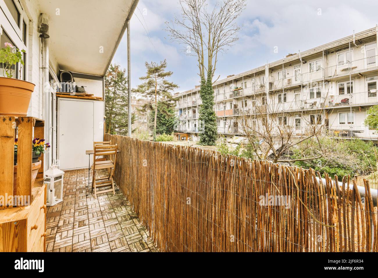 Narrow balcony with wooden railing with chair and table near flower
