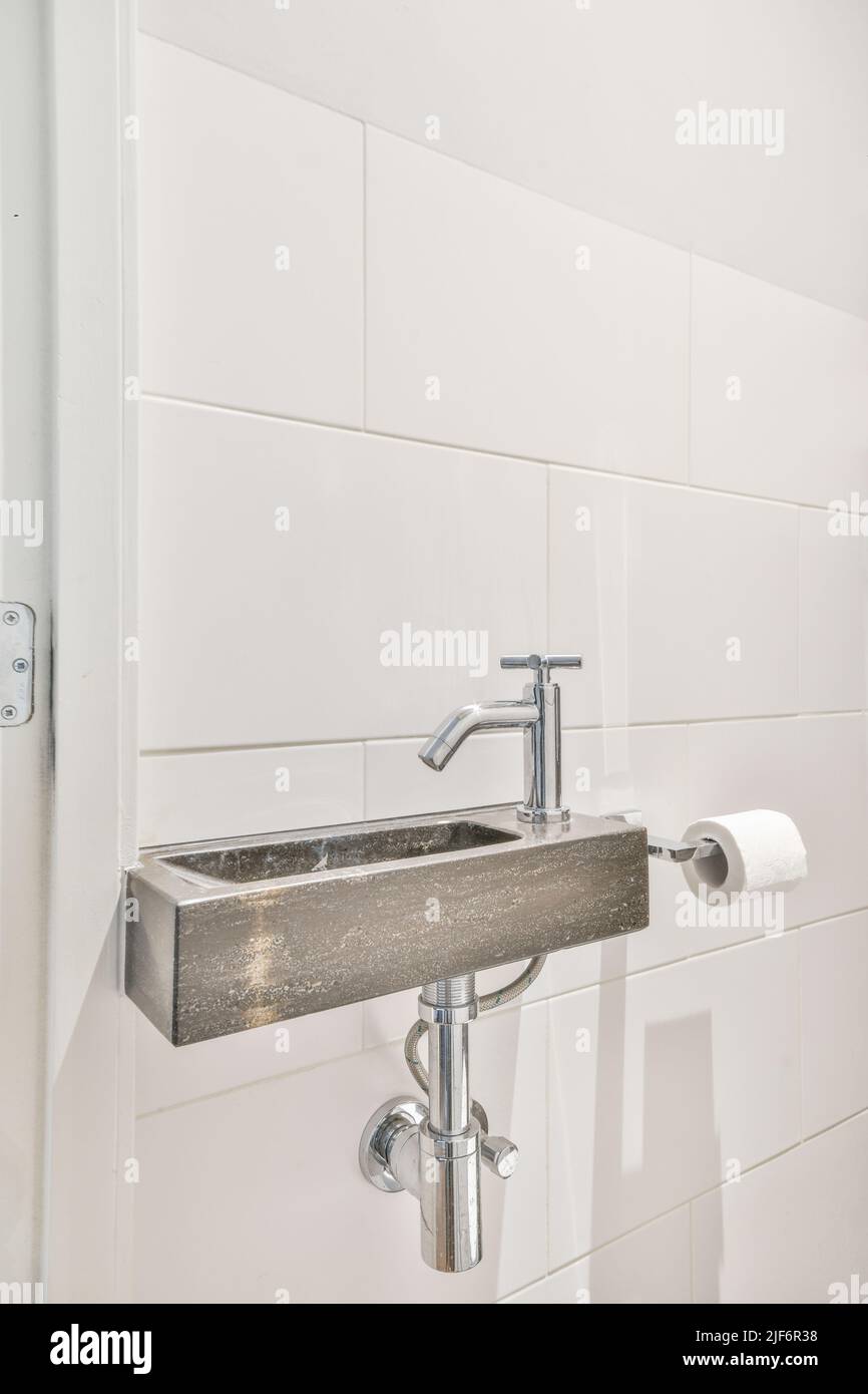 Ceramic sink attached to tiled wall near door and drying rack in modern restroom Stock Photo