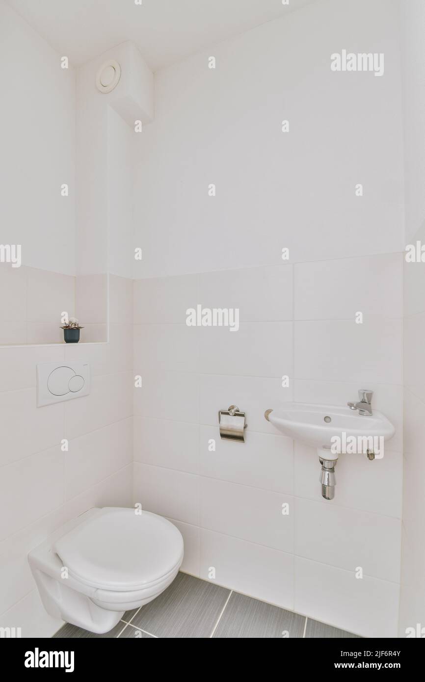 Wall hung toilet and small sink in corner in lavatory room with beige