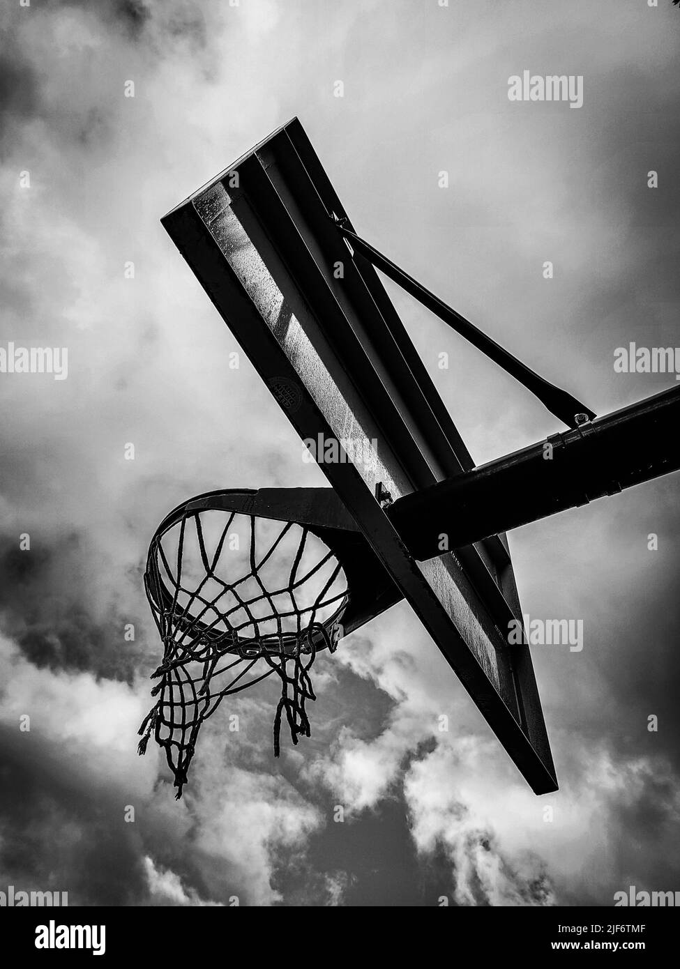 A low-angle and monochrome shot of the basketball hoop outlined against the sky Stock Photo