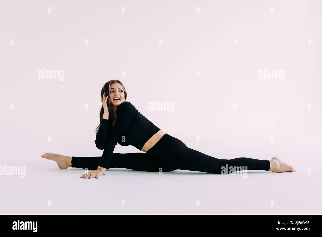 Flexible slim gymnast in black sportswear doing splits isolated on