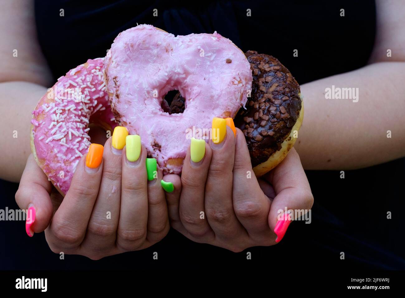 woman with fingernail extensions painted in variety of colours holding iced doughnuts Stock Photo