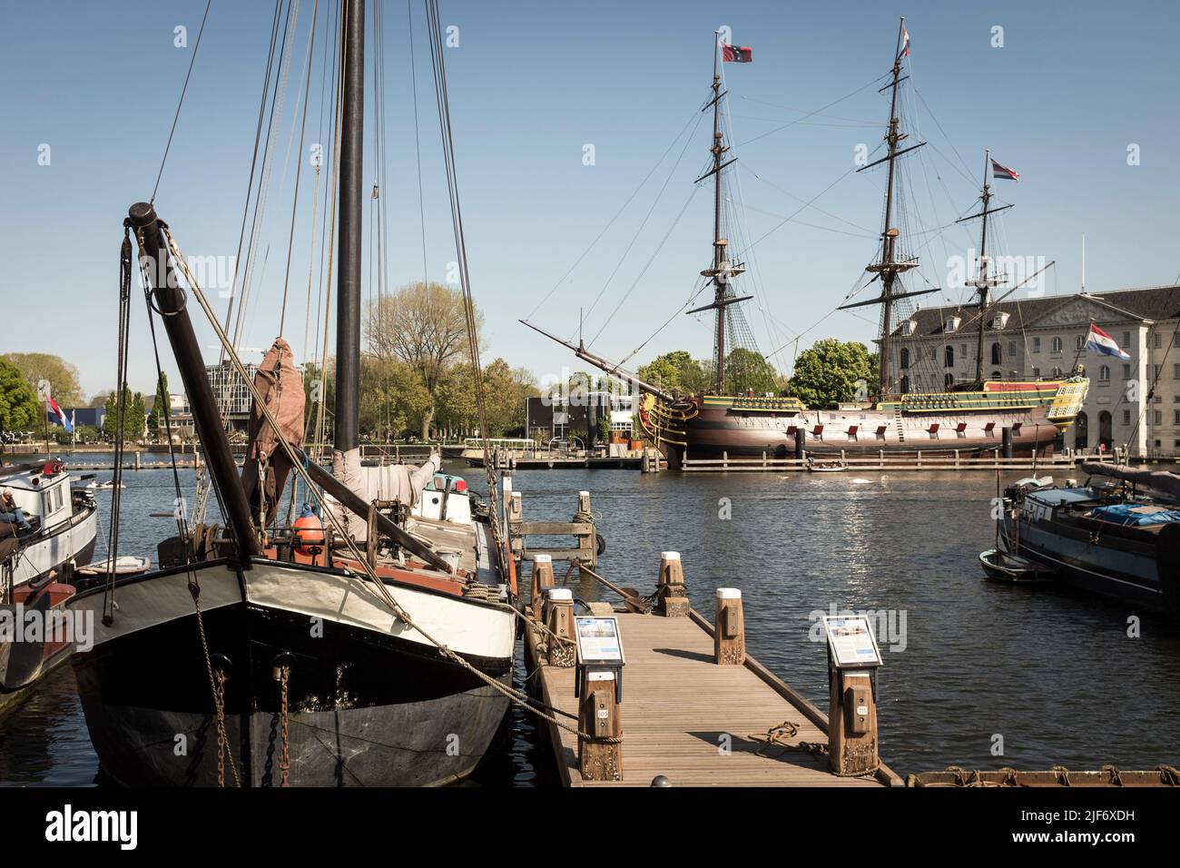 A replica of a Vereenigde Oostindische Compagnie, Dutch East India Company, ship, the Amsterdam, moored outside Het Scheepvaartmuseum, the National Maritime Museum, with a historic trading barge in the foreground, the Netherlands, in Amsterdam. Stock Photo