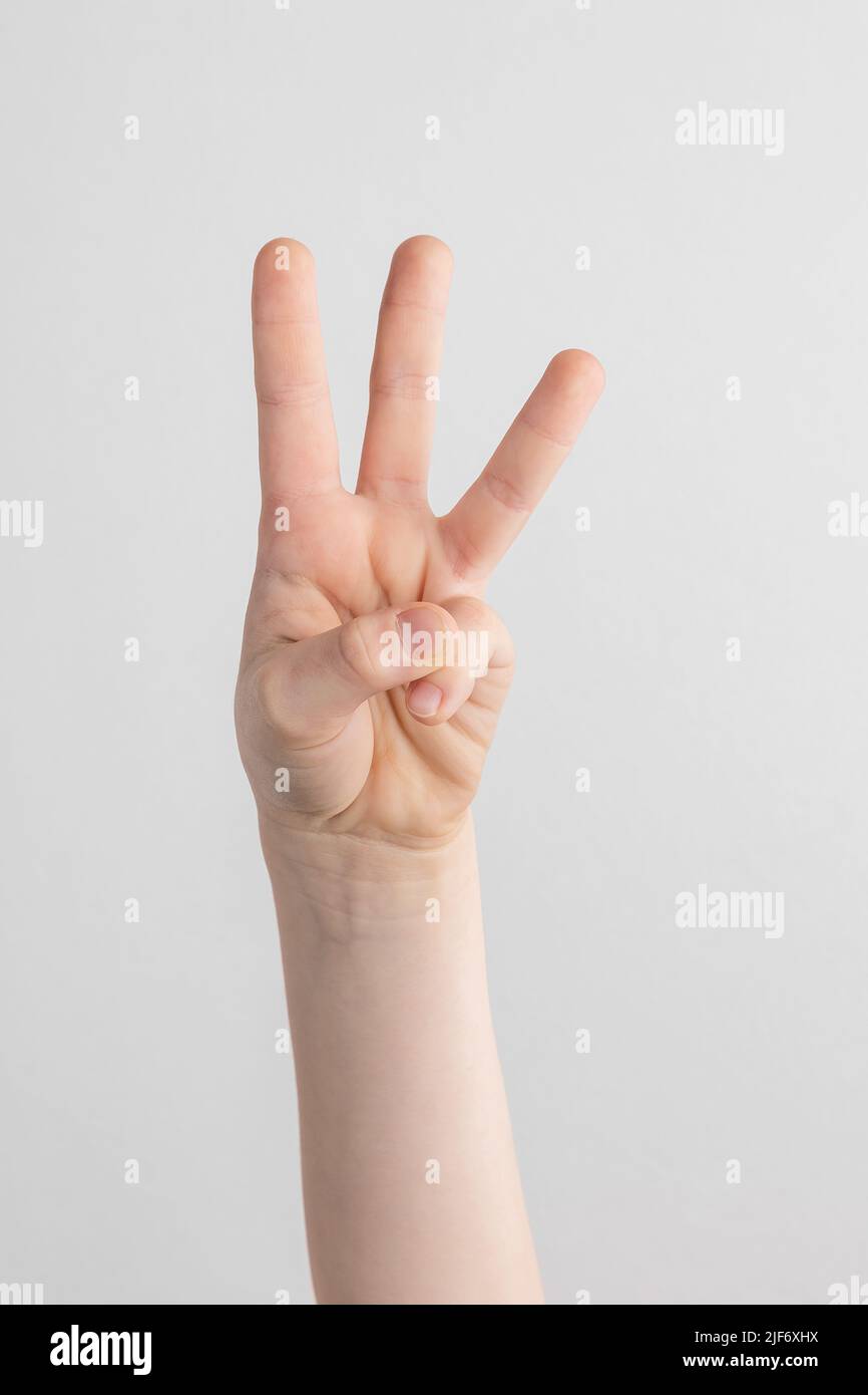 child hand counting and showing three fingers against white and gray background Stock Photo