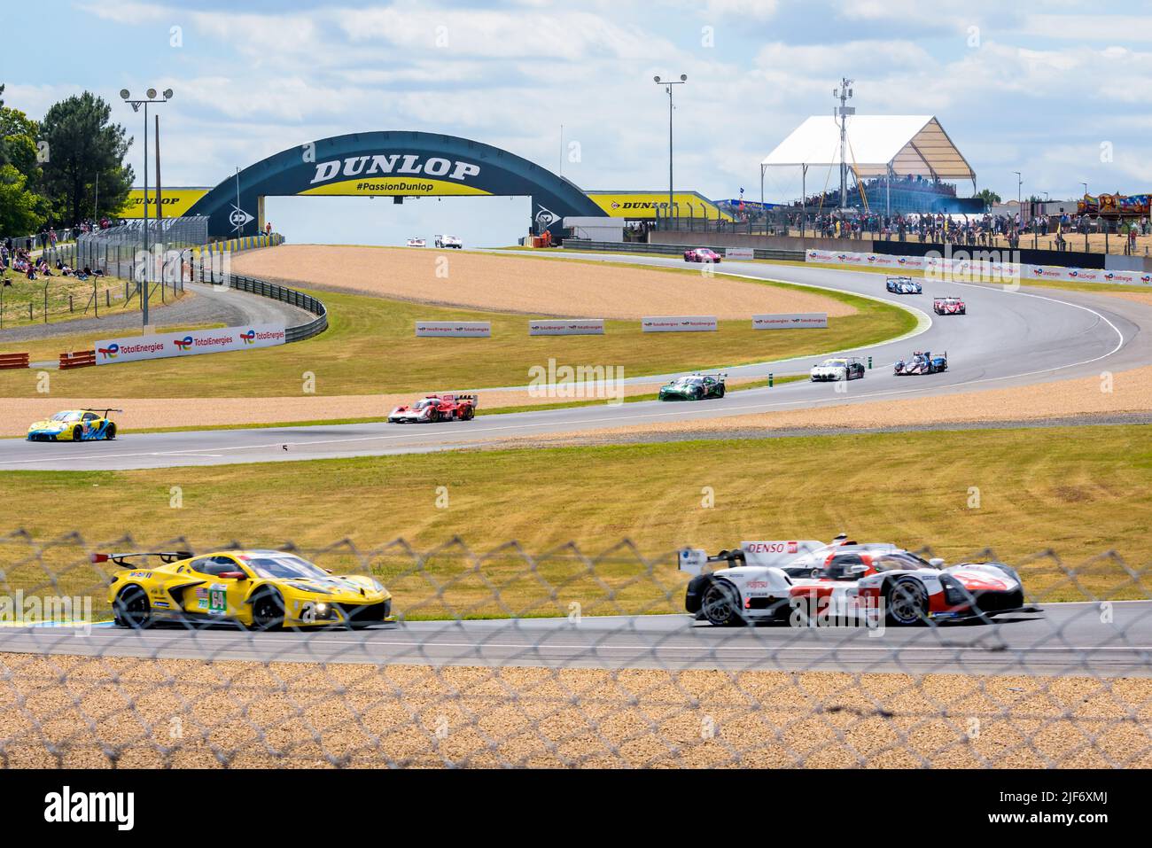 Race cars pass under the Dunlop footbridge and drive down the turns on the Circuit de la Sarthe racetrack during the 24 hours of Le Mans. Stock Photo