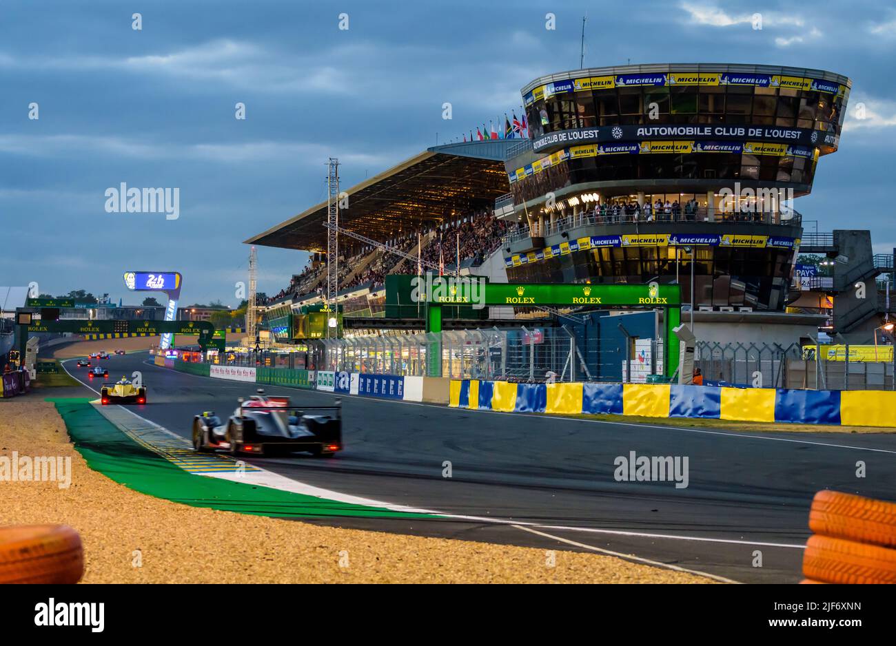 Prototype and GT race cars drive in the pit straight at nightfall on the Circuit de la Sarthe racetrack during the 24 hours of Le Mans. Stock Photo