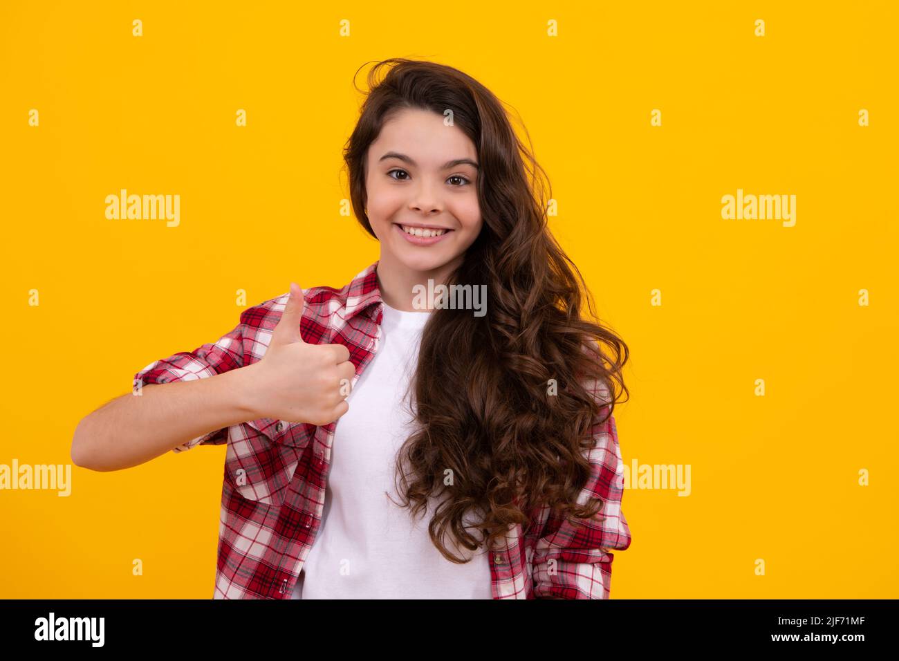 Happy teenager, positive and smiling emotions of teen girl. Optimistic cool teenager child girl with thumb up isolated on yellow background. Stock Photo