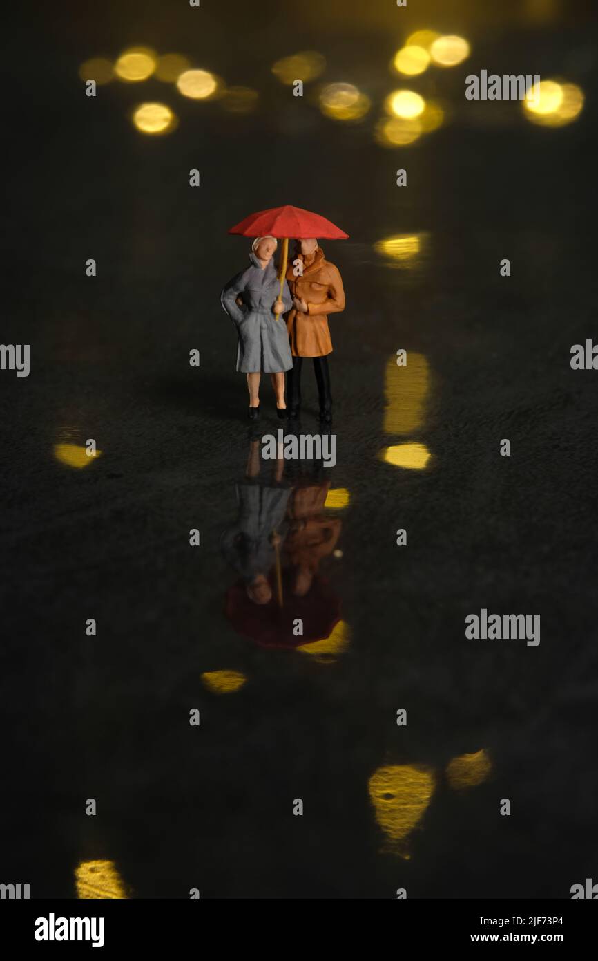 Miniature people toy figure photography. Couple dating at rainy day using umbrella at night. Beautiful golden yellow bokeh city light background. Imag Stock Photo