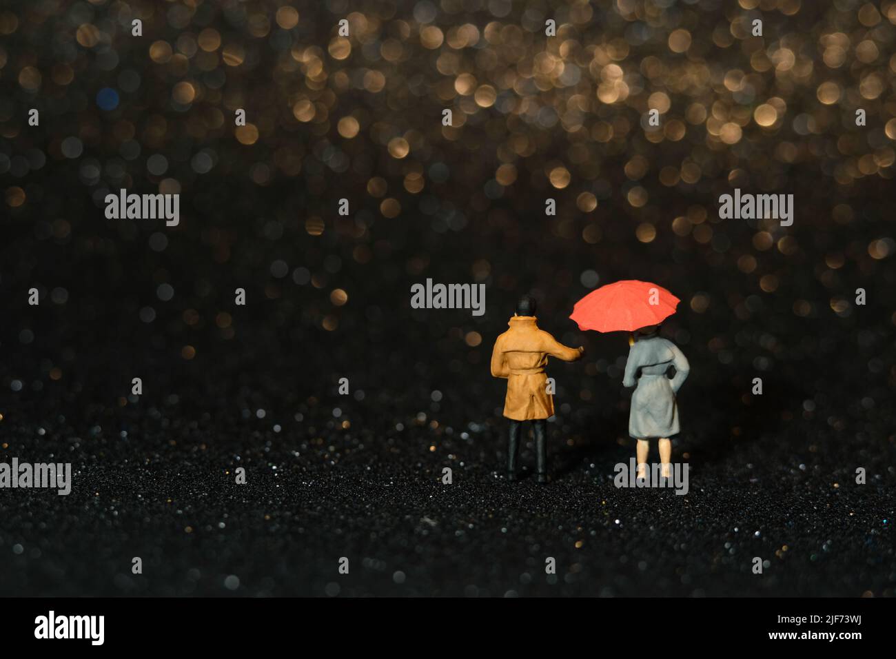 Miniature people toy figure photography. Couple dating at rainy day using umbrella at night. Beautifull golden yellow bokeh city light background. Ima Stock Photo