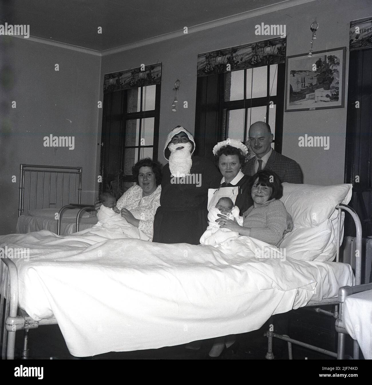 1965, historical, a father christmas visiting a maternity ward, standing for  a photo beisde a nurse and two new mothers lying in hospital beds with their new babies, Fife, Scotland, UK. Stock Photo