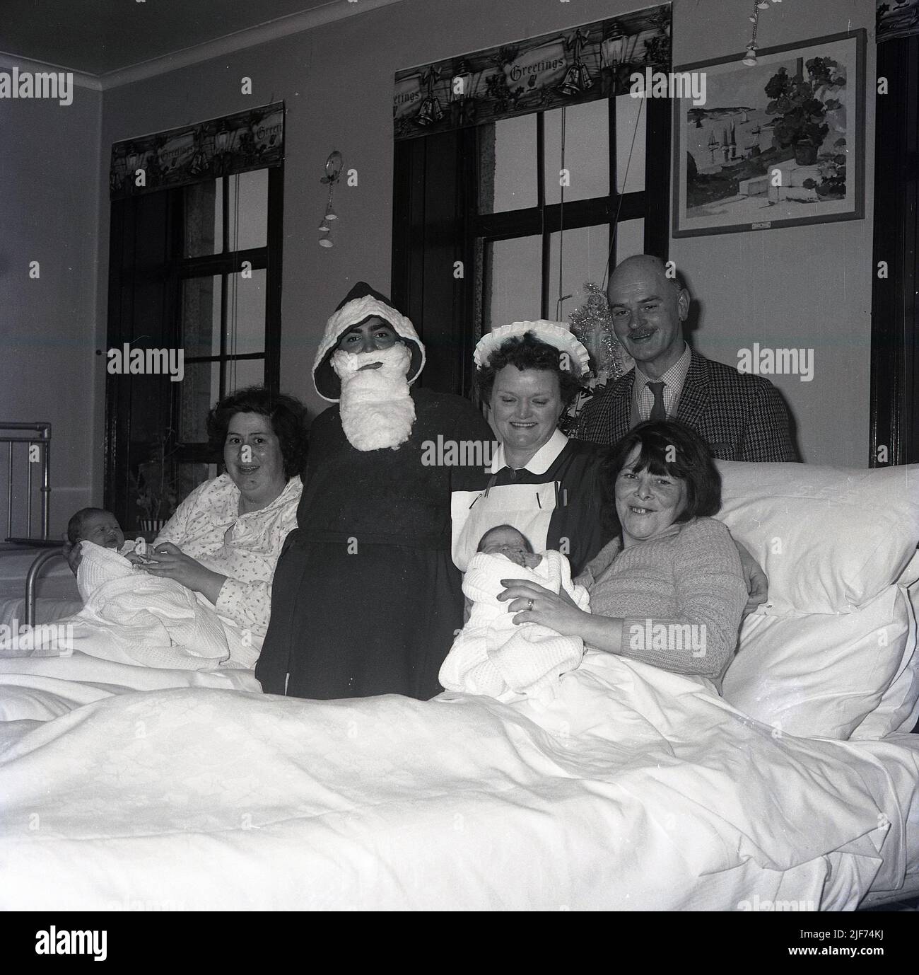 1965, historical, a father christmas visiting a maternity ward, standing for  a photo beisde a nurse and two new mothers lying in hospital beds with their new babies, Fife, Scotland, UK. Stock Photo