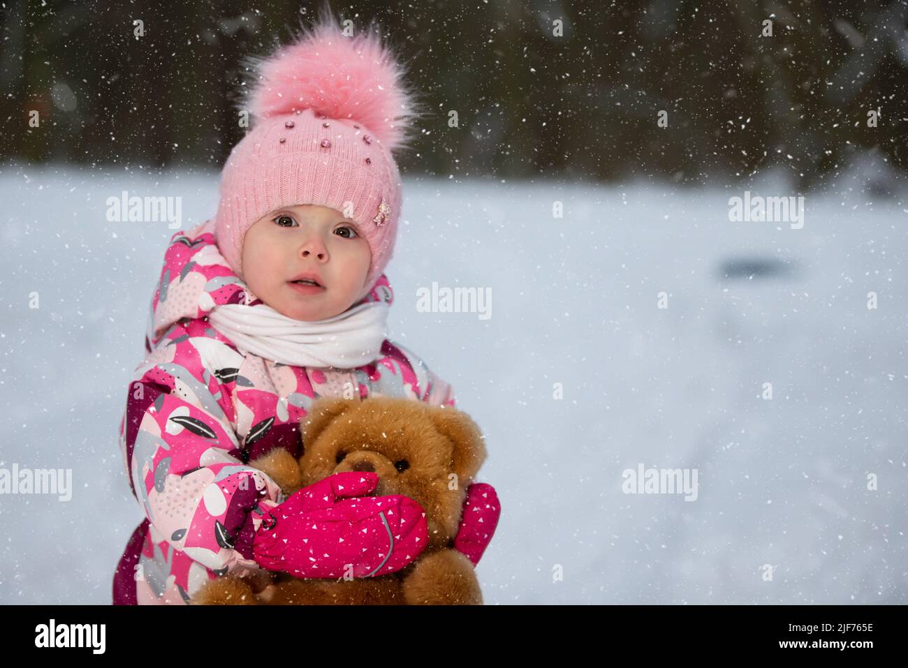 Little girl in winter with a teddy bear on the background of falling