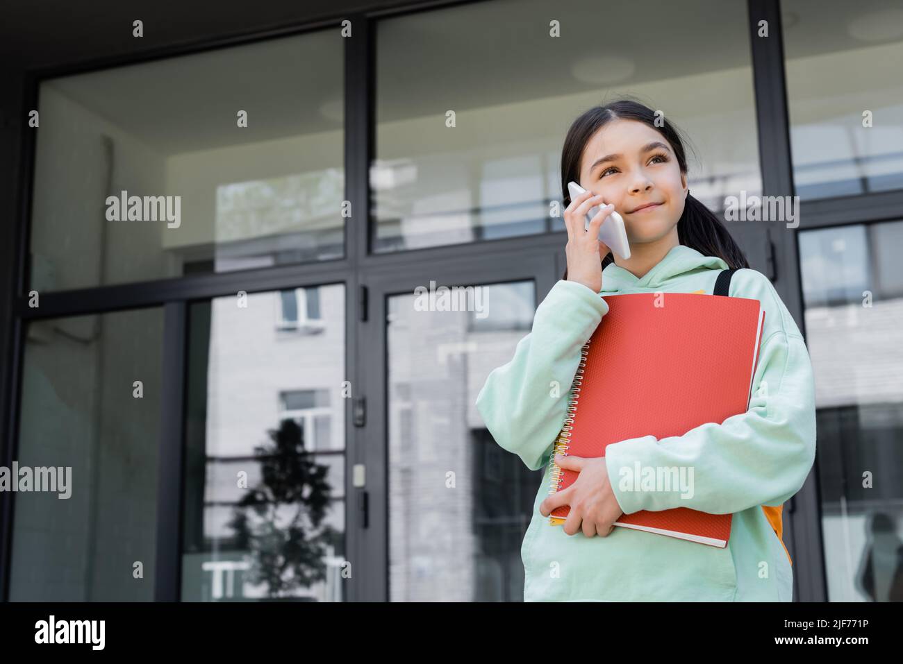 Schoolchild with notebooks talking on smartphone outdoors Stock Photo